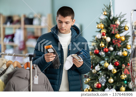 Male shopper in down jacket chooses warm socks in clothing store before Christmas Male shopper in down jacket chooses warm socks in clothing store before Christmas 137646906