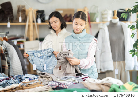 Mother and teen daughter looks at products in store and selects trousers Mother and teen daughter looks at products in store and selects trousers 137646916
