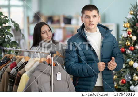 Guy tries on down jacket accompanied by girl in shop, X mas eve 137646919