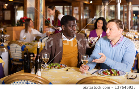 African American man calming upset friend in restaurant African American man calming upset friend in restaurant 137646923