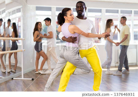 Middle-aged man and woman practicing tango dance in pair in training hall Middle-aged man and woman practicing tango dance in pair in training hall 137646931