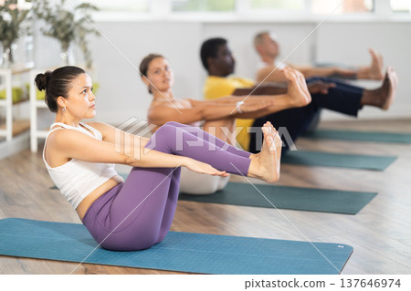 Young woman coach and students perform Paripurna Navasana during training in studio 137646974