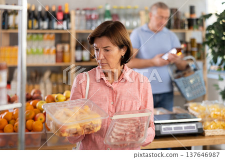 Woman chooses chicken or pork fillet, while her husband buys alcohol in supermarket Woman chooses chicken or pork fillet, while her husband buys alcohol in supermarket 137646987