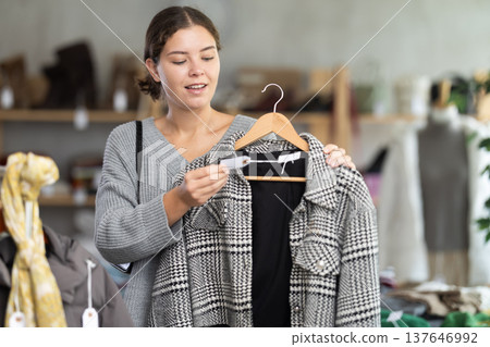 Interested young girl standing in clothing shop and looking new coat on sale of winter clothing collection 137646992