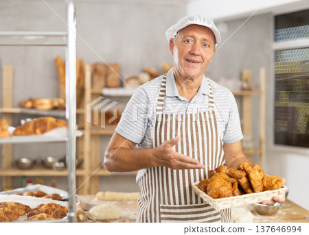 Bakery mature man employee holds basket of ready-made croissants. 137646994