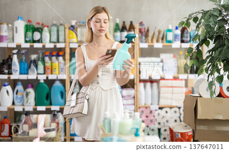 Checking expiration date of spray glass cleaner for windows - female shopper scans QR code on label of spray glass cleaner for windows using smartphone 137647011