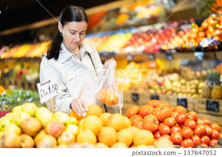 Focused positive middle aged woman shopping in organic food store, choosing oranges 137647052