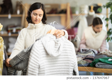 Adult woman chooses coat or down jacket in clothing store 137647067