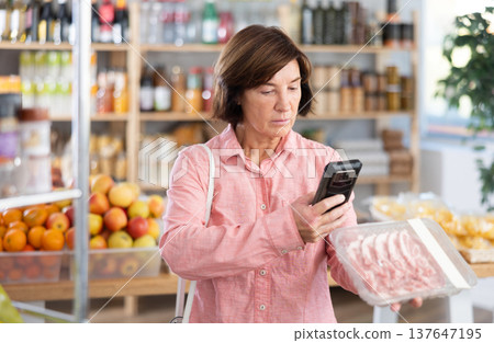 Mature woman is scanning QR on a package of pork in grocery 137647195