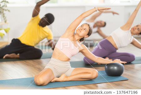 Multinational athletes sitting on floor in asana pigeon do body tilts to side, use fitball 137647196