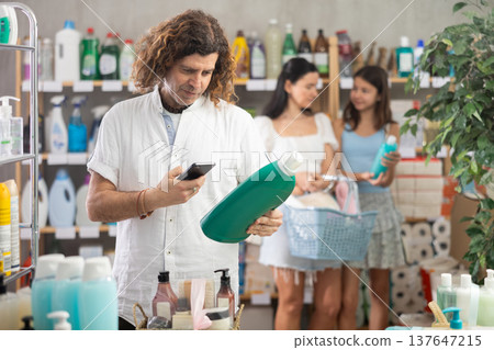 Man scanning QR-code on detergent, mom and daughter doing shopping Man scanning QR-code on detergent, mom and daughter doing shopping 137647215