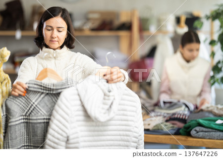 Woman looks at products in store and selects coat or jacket. Family shopping Woman looks at products in store and selects coat or jacket. Family shopping 137647226