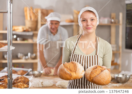 Bakery girl employee holds ready-made loafs of bread. Bakery girl employee holds ready-made loafs of bread. 137647246