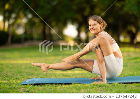 Sporty girl doing arm balancing Elephant Trunk Pose in summer park 137647248