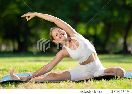 Young woman practicing yoga on green glade in summer park 137647249