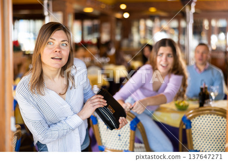 Female thief stealing handbag of frightened woman in restaurant Female thief stealing handbag of frightened woman in restaurant 137647271