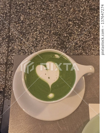 Matcha latte in a clear cup with vibrant green color, topped with creamy froth, highlighting smooth texture, swirling patterns, and refreshing appearance in close-up detail 137647274