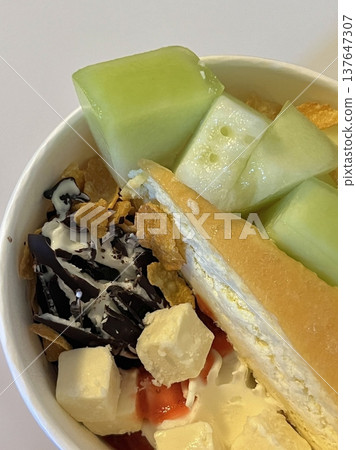 Swirled yogurt ice cream dessert served in a cup, smooth creamy texture with glossy surface, topped with fresh fruit pieces, highlighting its refreshing and inviting appearance in detail Swirled yogurt ice cream dessert served in a cup, smooth creamy texture with glossy surface, topped with fresh fruit pieces, highlighting its refreshing and inviting appearance in detail 137647307