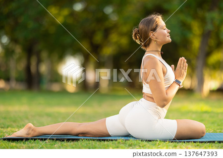 Girl in park on green grass of lawn performs hatha yoga 137647393