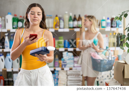 Young girl in summer clothes scanning QR-code on cleaning spray other choosing something Young girl in summer clothes scanning QR-code on cleaning spray other choosing something 137647436