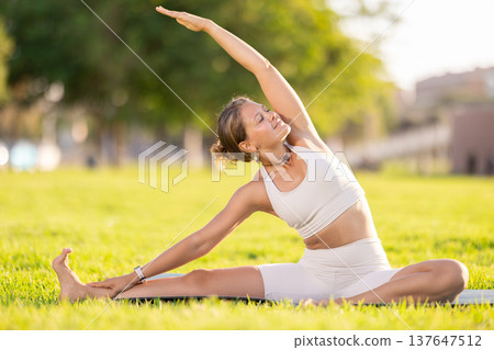 Girl in park on green grass of lawn performs Parivritta Janu Shirshasana 137647512