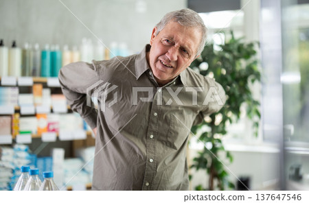 Older man experiencing sharp back pain while shopping in pharmacy 137647546