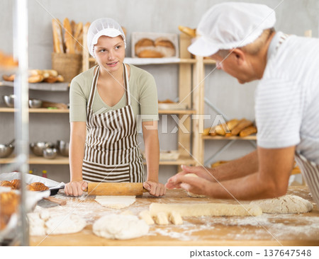 Elderly baker teaches young girl how to make raw dough - rolling it out with rolling pin 137647548
