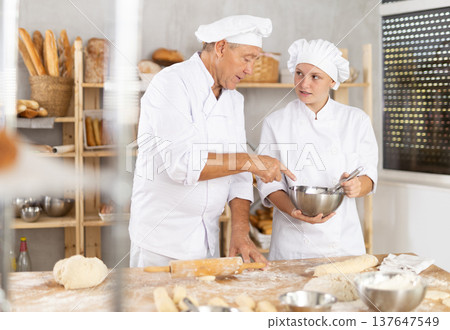 Older baker teaching young female apprentice in bakery 137647549
