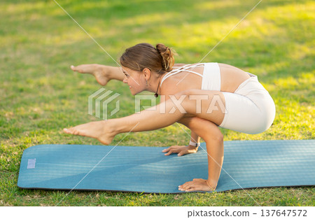 Girl in park on green grass of lawn performs Bhujapidasana Girl in park on green grass of lawn performs Bhujapidasana 137647572