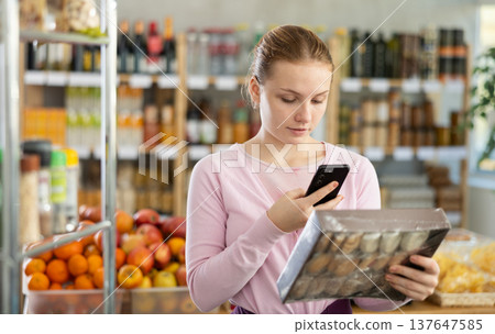 Female shopper scanning QR code on cookies label in grocery department of supermarket Female shopper scanning QR code on cookies label in grocery department of supermarket 137647585