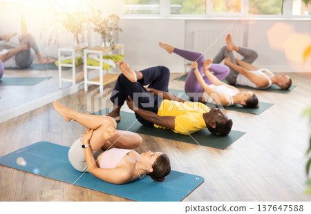 Young woman coach and students perform Supta kapotasana during training in studio Young woman coach and students perform Supta kapotasana during training in studio 137647588
