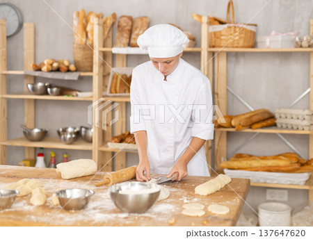 Young female baker cutting dough with scraper 137647620