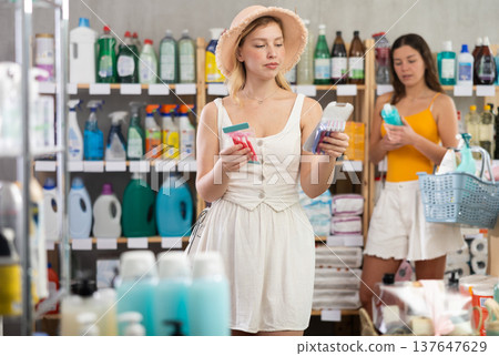 Woman consumer choose razor in household supermarket, while in background shoppers browse products 137647629