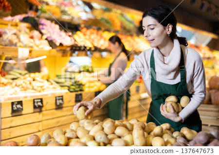 Young woman seller puts potatoes in vegetable shop Young woman seller puts potatoes in vegetable shop 137647673