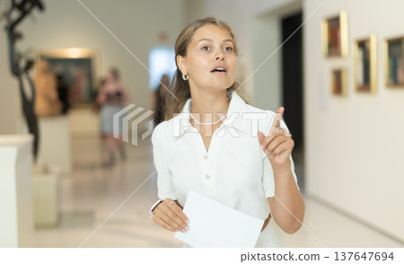 Portrait of young girl visitor with paper guide at the exhibition of paintings in museum Portrait of young girl visitor with paper guide at the exhibition of paintings in museum 137647694