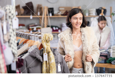 Woman try on fur jacket in front of mirror in clothes store, semi naked body Woman try on fur jacket in front of mirror in clothes store, semi naked body 137647735