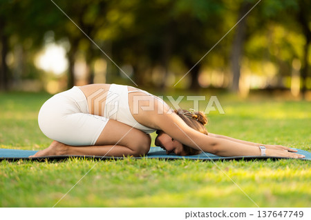 Young woman doing restful yoga pose Balasana in summer park Young woman doing restful yoga pose Balasana in summer park 137647749