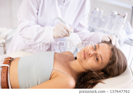 Young female patient undergoing facial skin cleansing with ultrasonic shovel Young female patient undergoing facial skin cleansing with ultrasonic shovel 137647762