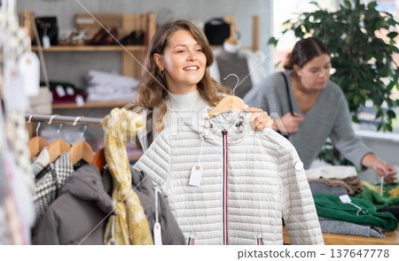 Girl chooses fashionable down jacket in clothing boutique 137647778