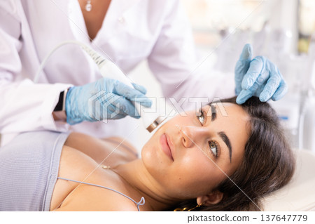 Female patient receiving facial procedure with ultrasonic vibration attachment 137647779
