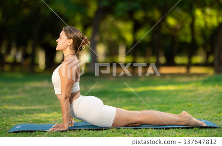 Girl doing Upward Facing Dog yoga pose in summer park Girl doing Upward Facing Dog yoga pose in summer park 137647812