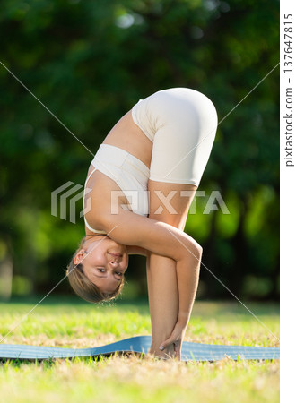 Girl in park on green grass of lawn performs Uttanasana Girl in park on green grass of lawn performs Uttanasana 137647815