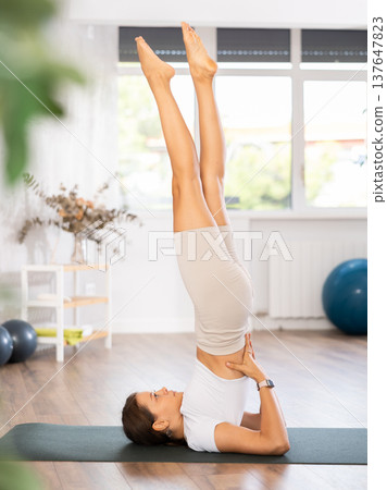 Young woman yoga trainer performing shoulderstand pose on black rug 137647823