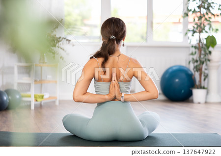Young woman yoga trainer performing lotus pose variation on black rug 137647922