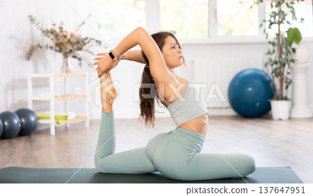 Young woman yoga trainer performing king pigeon pose on black rug 137647951