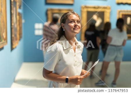 Woman with sheet piece of paper in hands view pictures and icons in museum hall Woman with sheet piece of paper in hands view pictures and icons in museum hall 137647953