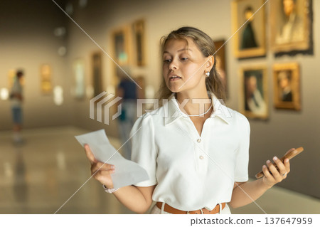 Woman with phone in hands view pictures and icons in museum hall Woman with phone in hands view pictures and icons in museum hall 137647959