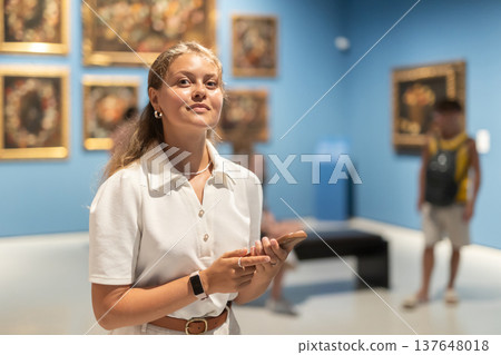 Portrait of young attractive woman holding an information booklet during a visit to fine arts museum Portrait of young attractive woman holding an information booklet during a visit to fine arts museum 137648018