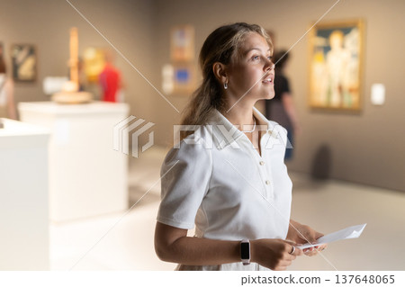 Woman with sheet piece of paper in hands view pictures and icons in museum hall Woman with sheet piece of paper in hands view pictures and icons in museum hall 137648065