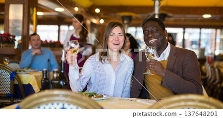 Cheerful woman with african american friend having dinner in restaurant Cheerful woman with african american friend having dinner in restaurant 137648201